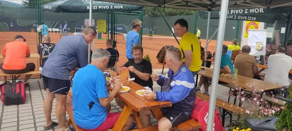 Účastníci turnaje sedí společně u stolů pod stanem.
